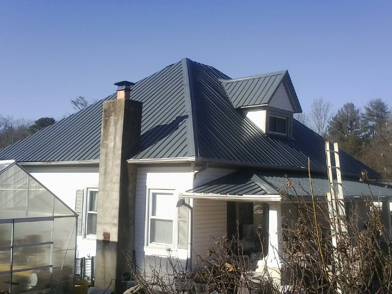 Dark blue standing seam metal roof on a white farmhouse with dormer — Slate & Tile Roof Repair by Roofing Brothers in Lawndale