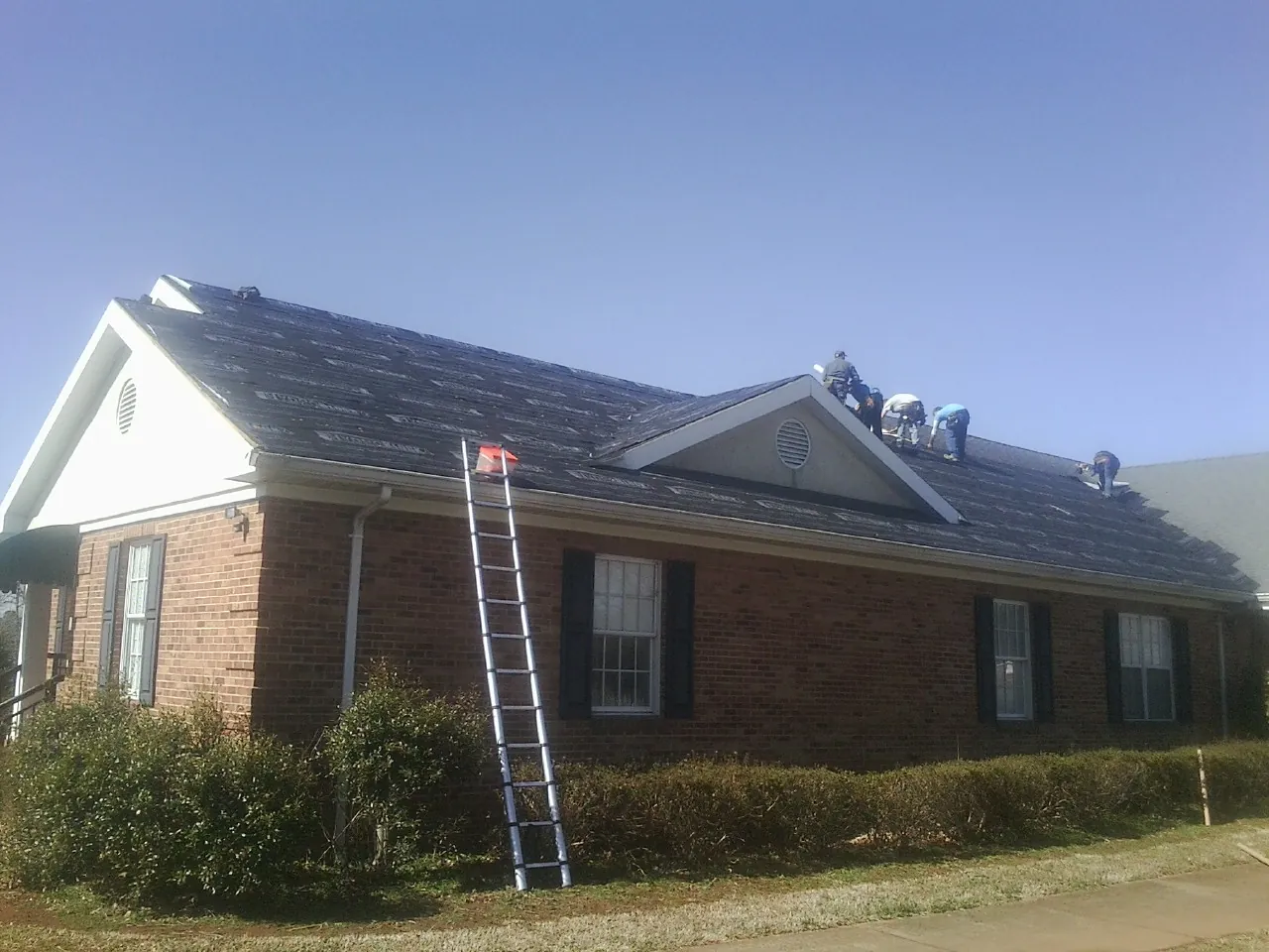 Crew tearing shingles off a brick ranch roof with a ladder set — Emergency Roof Repair work by our crew in Lawndale