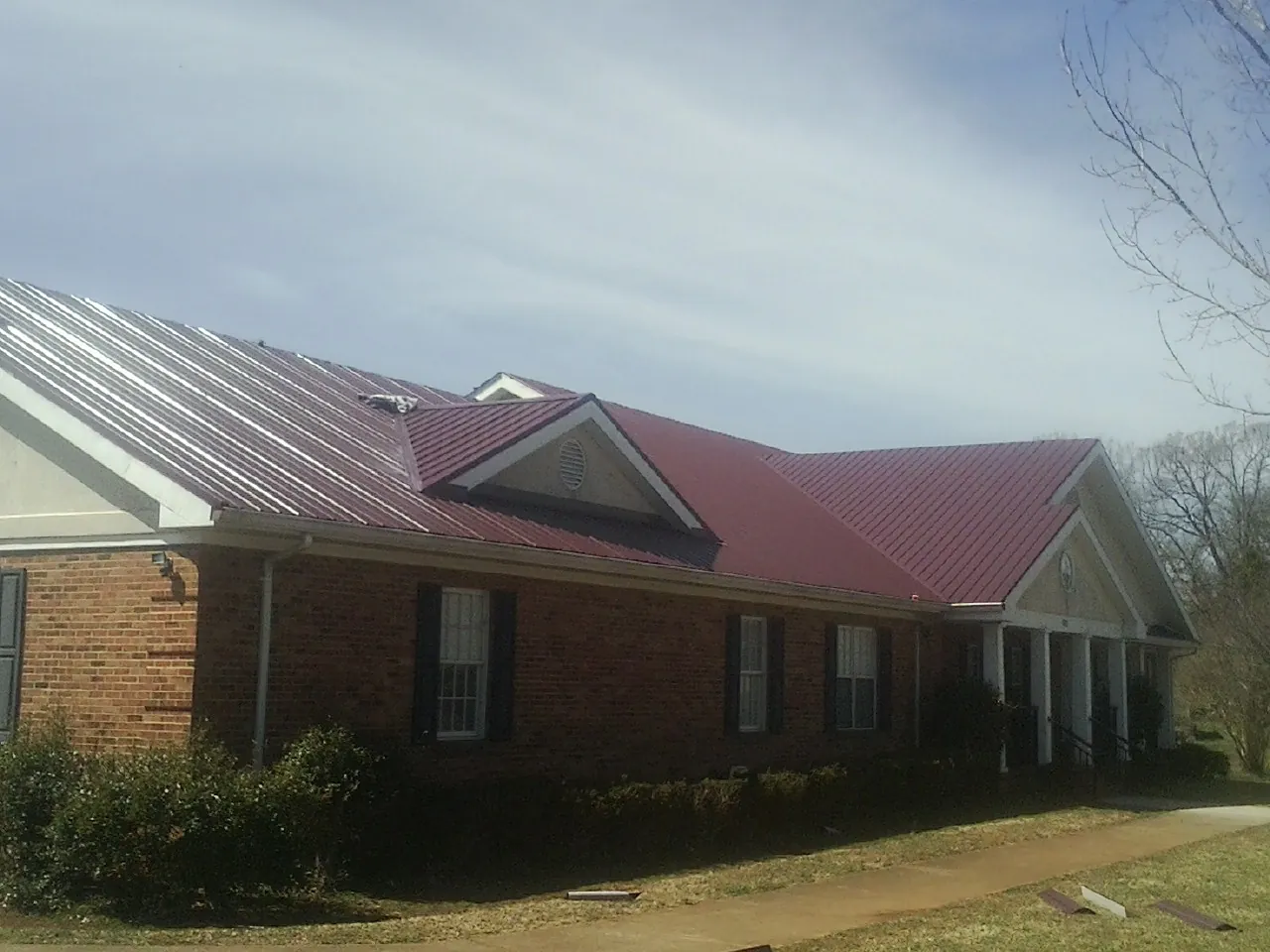 Red metal roof with gabled entries on a long brick building, from a Hail Damage Roof Repair job in Lawndale