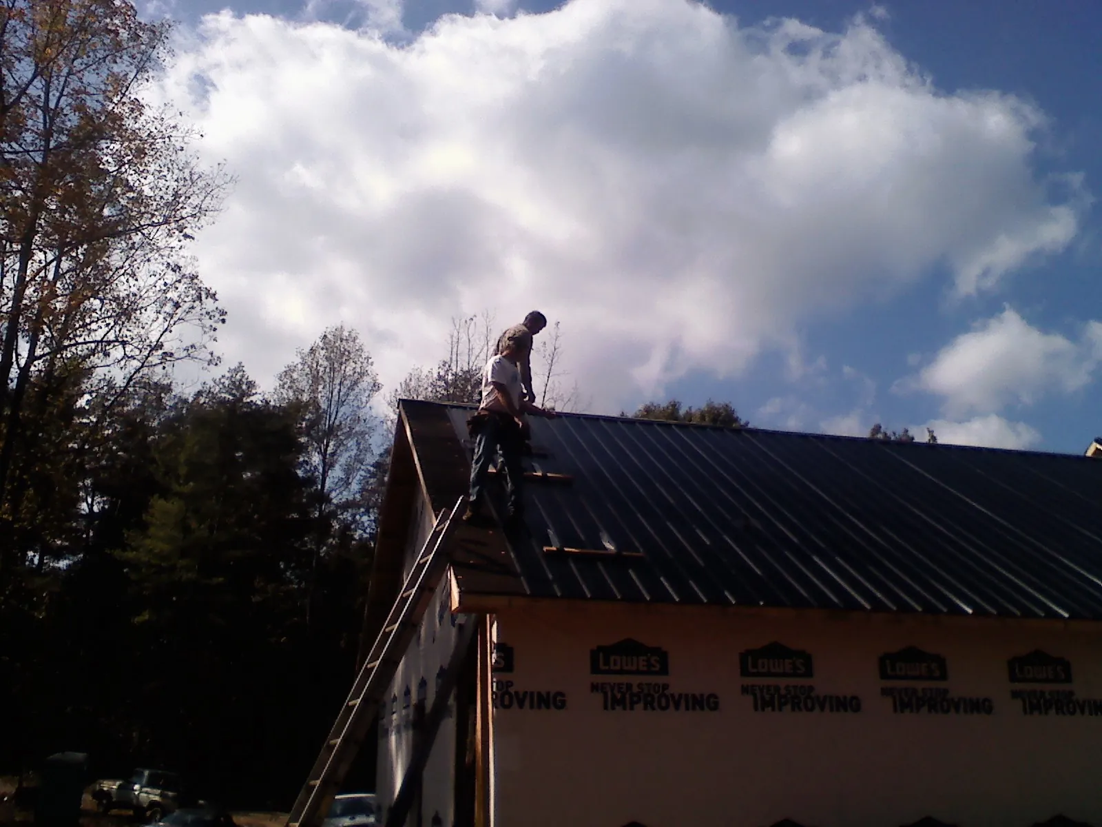 Roofer fastening dark metal panels high against a cloudy sky, from a Roof Inspection job in Lawndale