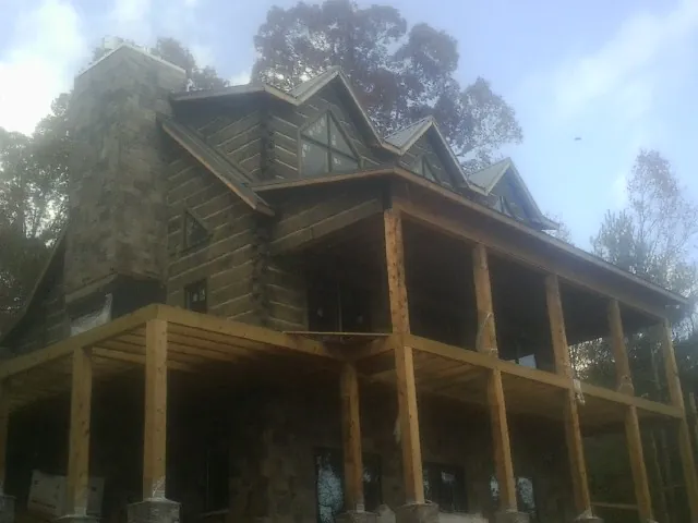 Stone chimney and dormers on a large log home with a timber porch in Lawndale